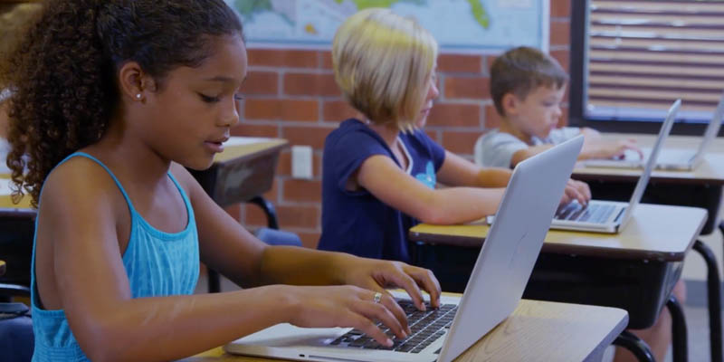 Three children on laptops in a school setting.