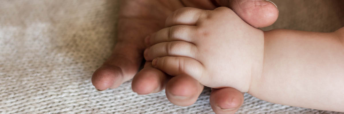 An older adult hand holding a newborn's hand.